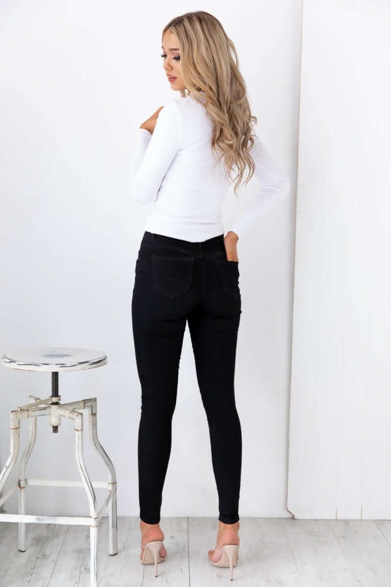 Model wearing black Justified Jeans with mid-high waist and skinny fit, paired with a white top and stylish heels.