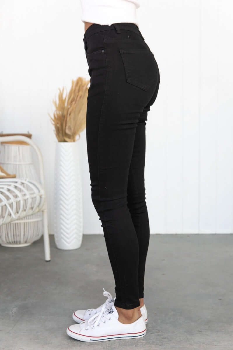 Skinny fit black Justified Jeans with mid-high waist and pockets, styled with classic white sneakers.