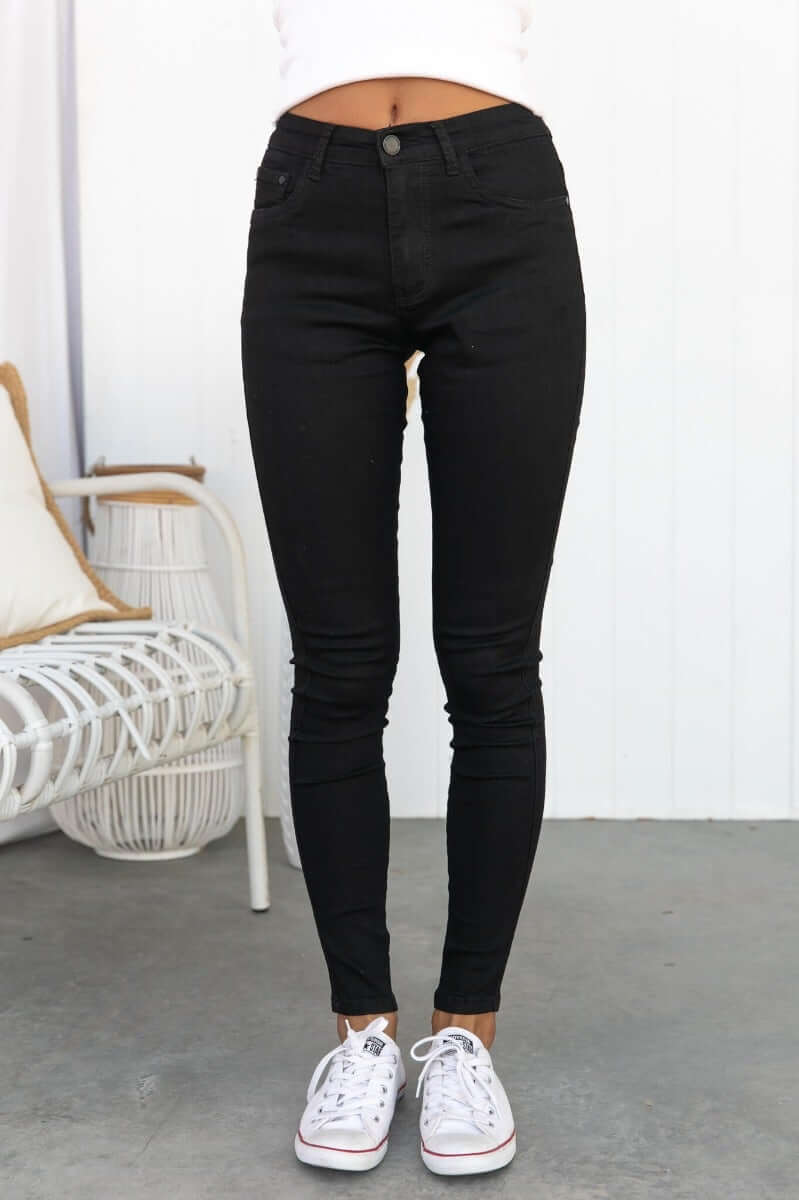 Model wearing Justified Jeans, black mid-high waist skinny fit with pockets, styled with white sneakers.