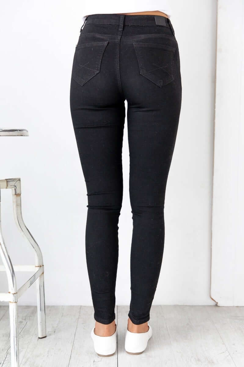 Back view of Justified Jeans in black, featuring a mid-high waist fit and pockets, showcasing a skinny fit style.