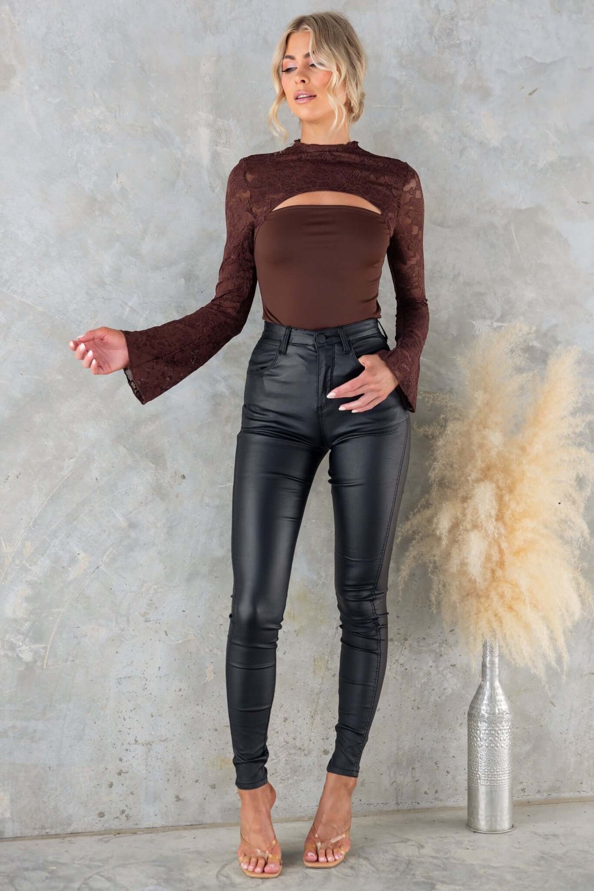 Model wearing Kaiya Top with mock neckline and cut-out, paired with black high-waisted pants against a textured backdrop.