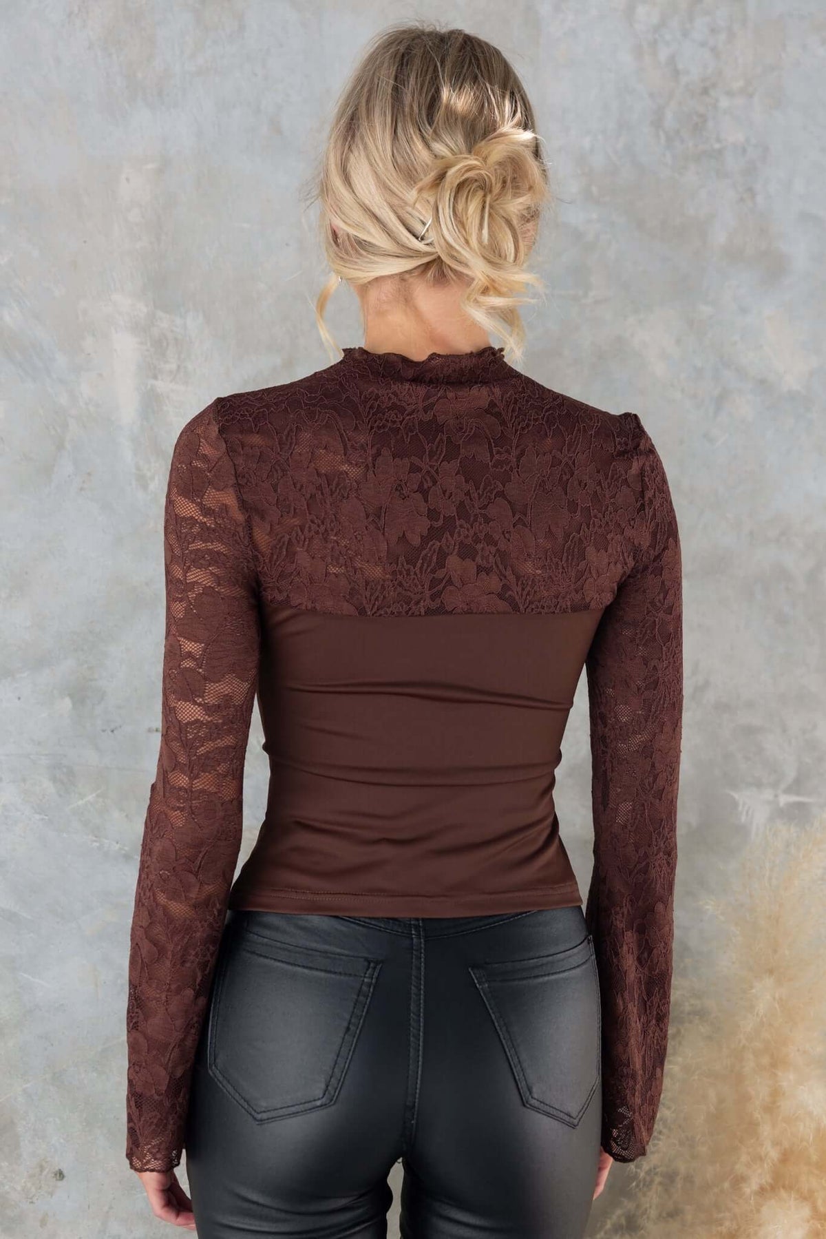 Back view of the Kaiya Top featuring a mock neckline and lace panel in brown, styled with black leather pants.
