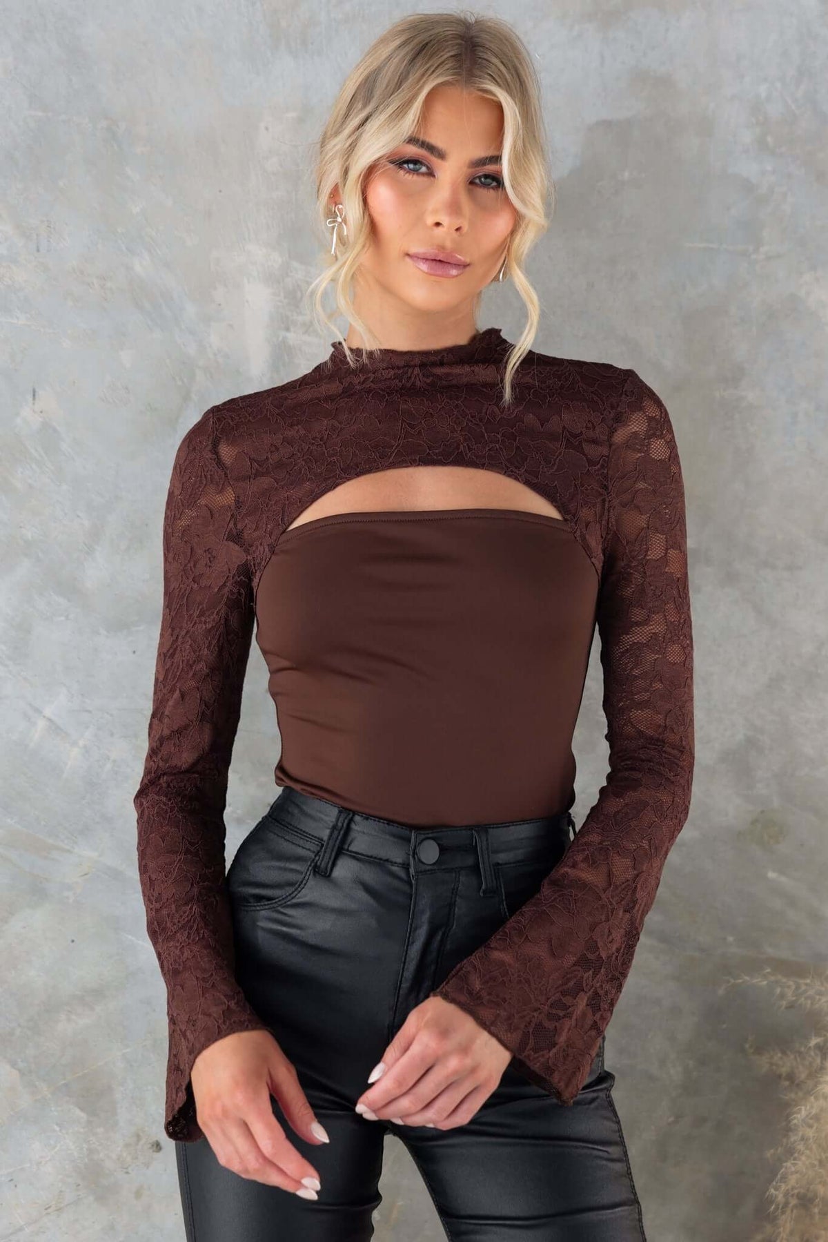 Stylish Kaiya Top in brown with mock neckline, cut-out bust, and lace panel, worn by model with black leather pants.