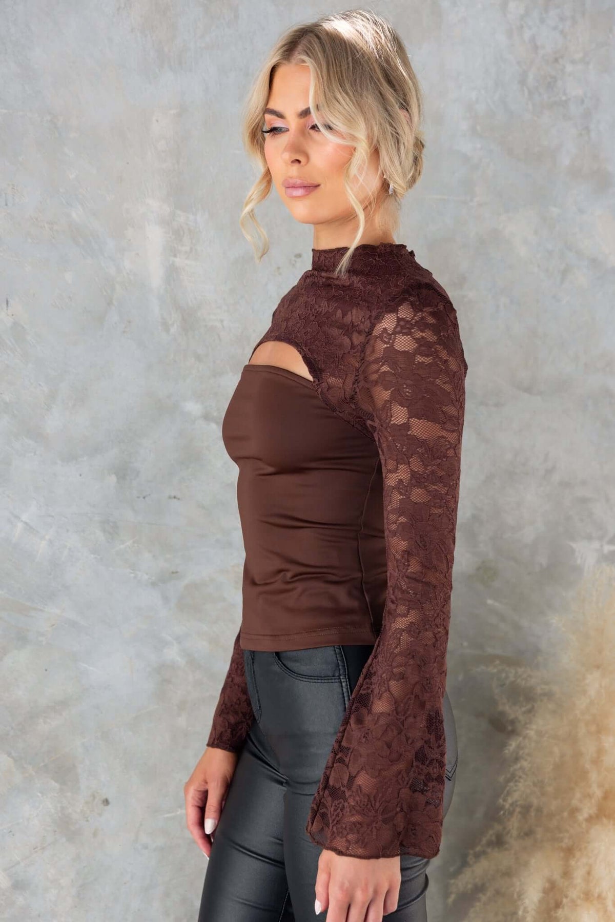 Kaiya Top featuring a mock neckline, lace panel, and cut-out detail at the bust, styled with pants.