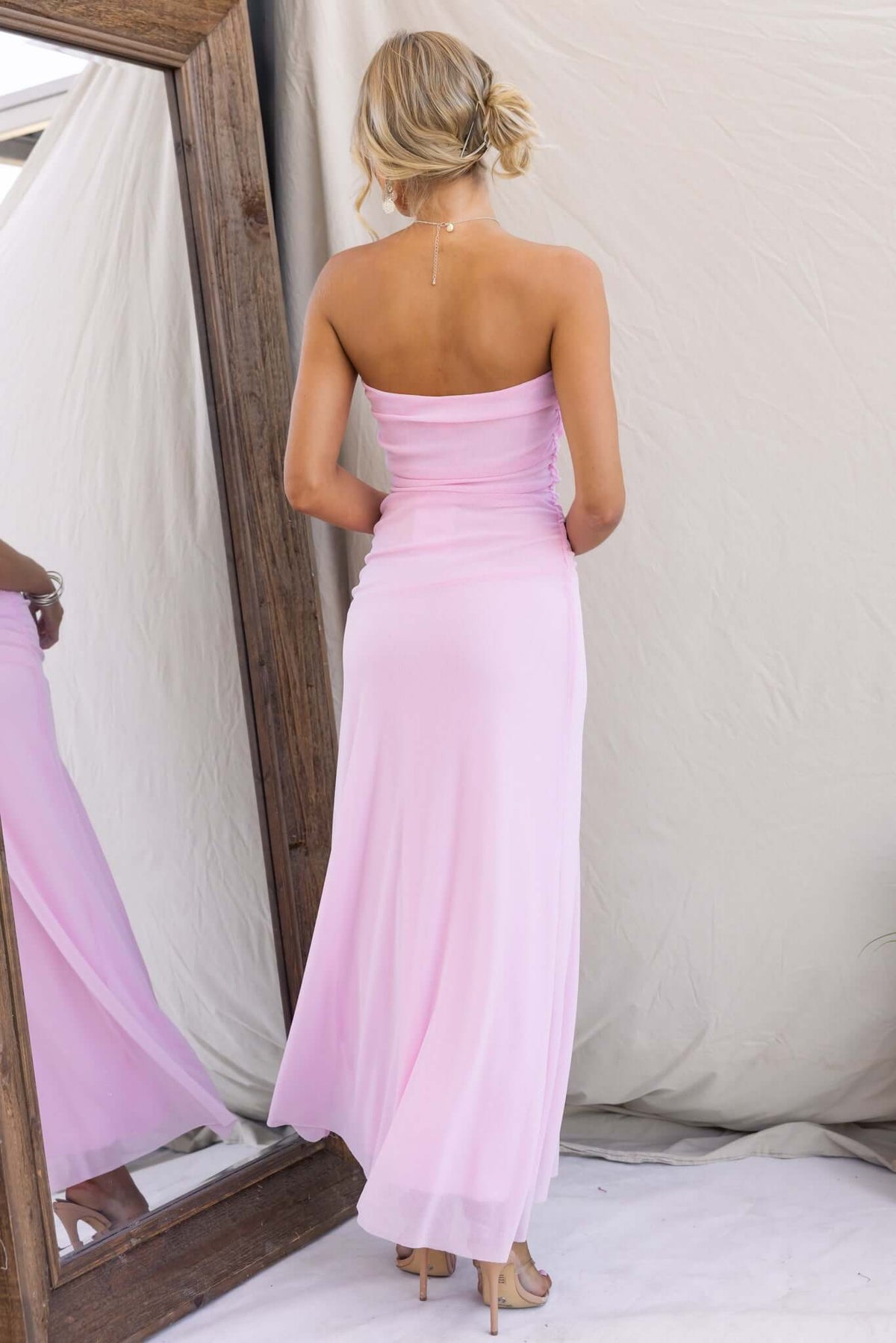 Back view of a model in a pink strapless maxi dress with a split, showcasing stretchy fabric and elegant design.