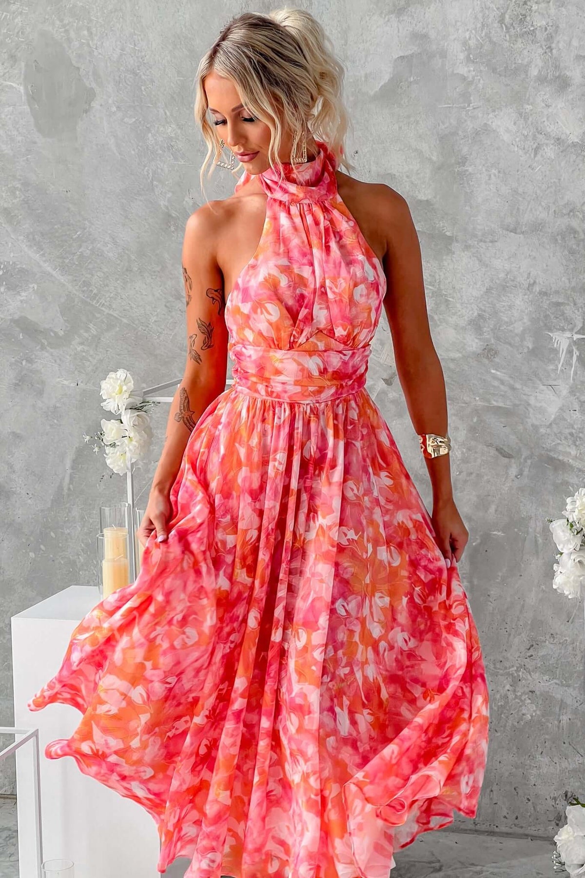 Model in a pink and coral floral maxi dress with a high tie neckline, showcasing a flowing skirt and elegant design.