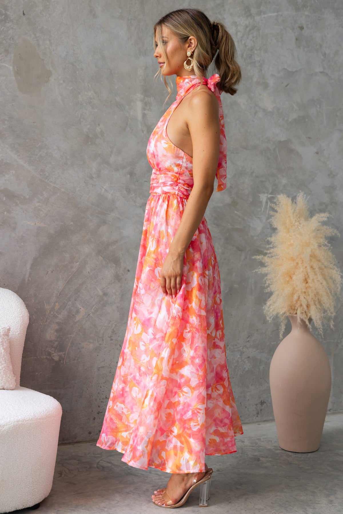 Model wearing a vibrant pink floral Little Things Maxi Dress with a high tie neckline and flowing skirt.