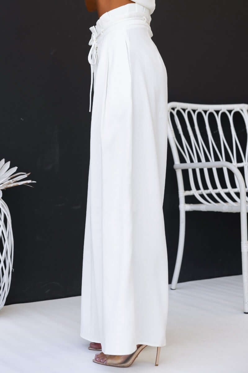 Model wearing white long shot pants with a paperbag waist and removable tie, highlighting pockets and a stylish fit.