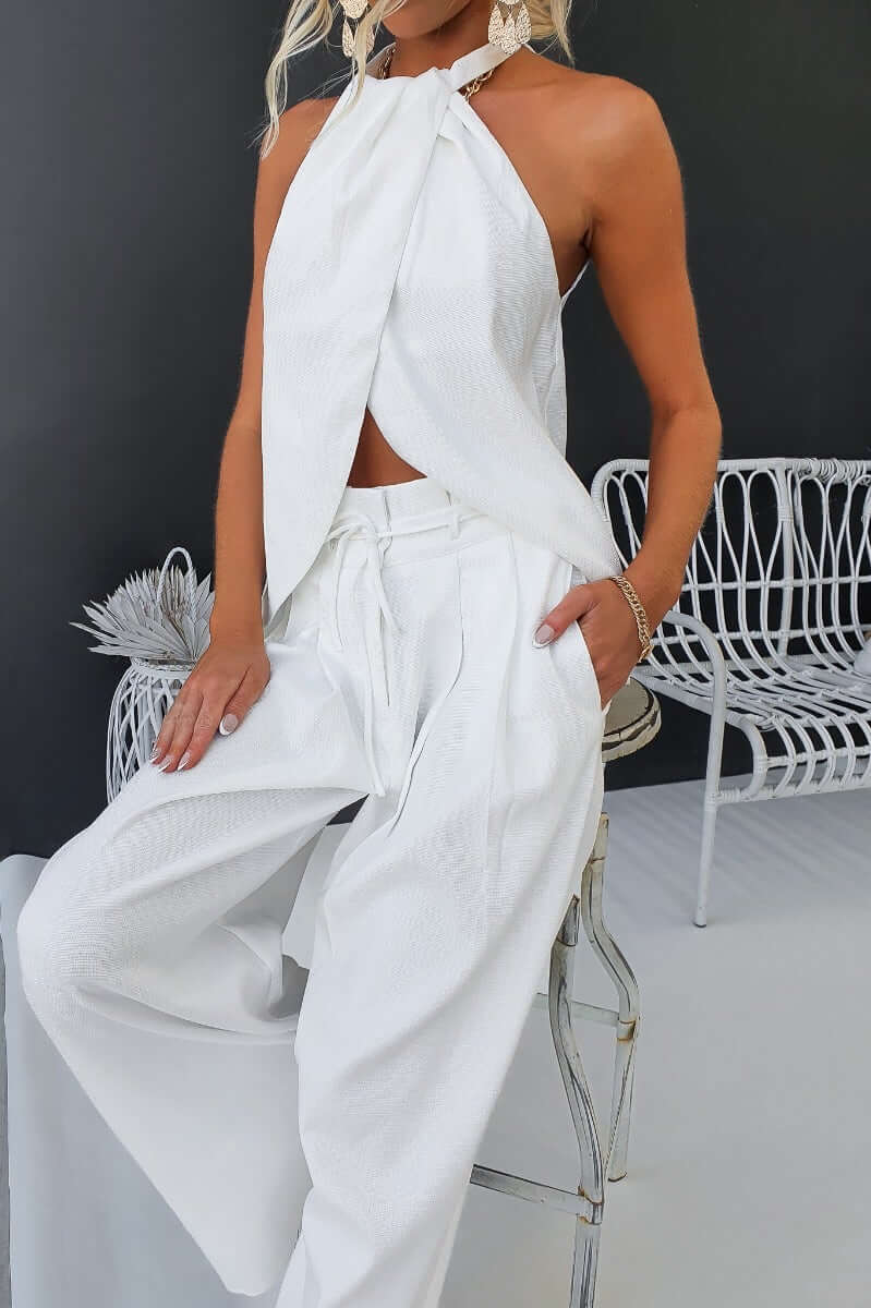 Stylish woman in a white halter top and long shot pants with paperbag waist sitting on a chair.