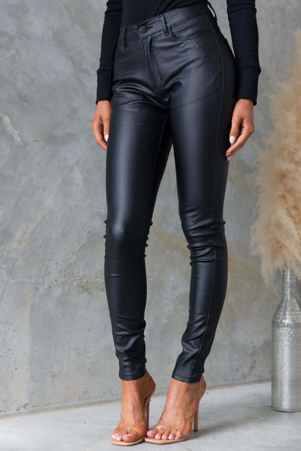 Luscious black faux leather pants with mid to high waist fit, showcased on a model in stylish heels.