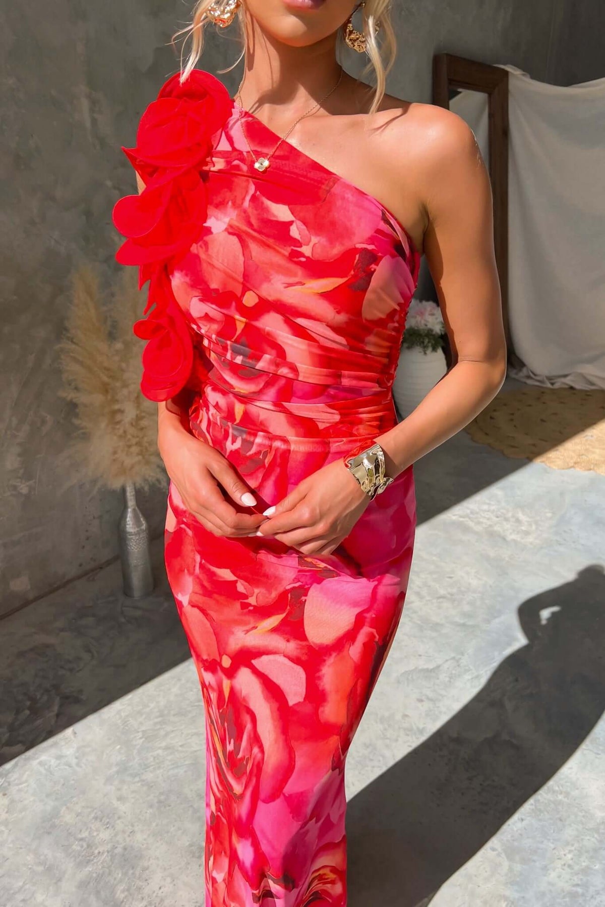 Model in a vibrant floral one-shoulder maxi dress with mesh detail and side zip, showcasing a bright red and pink color palette.