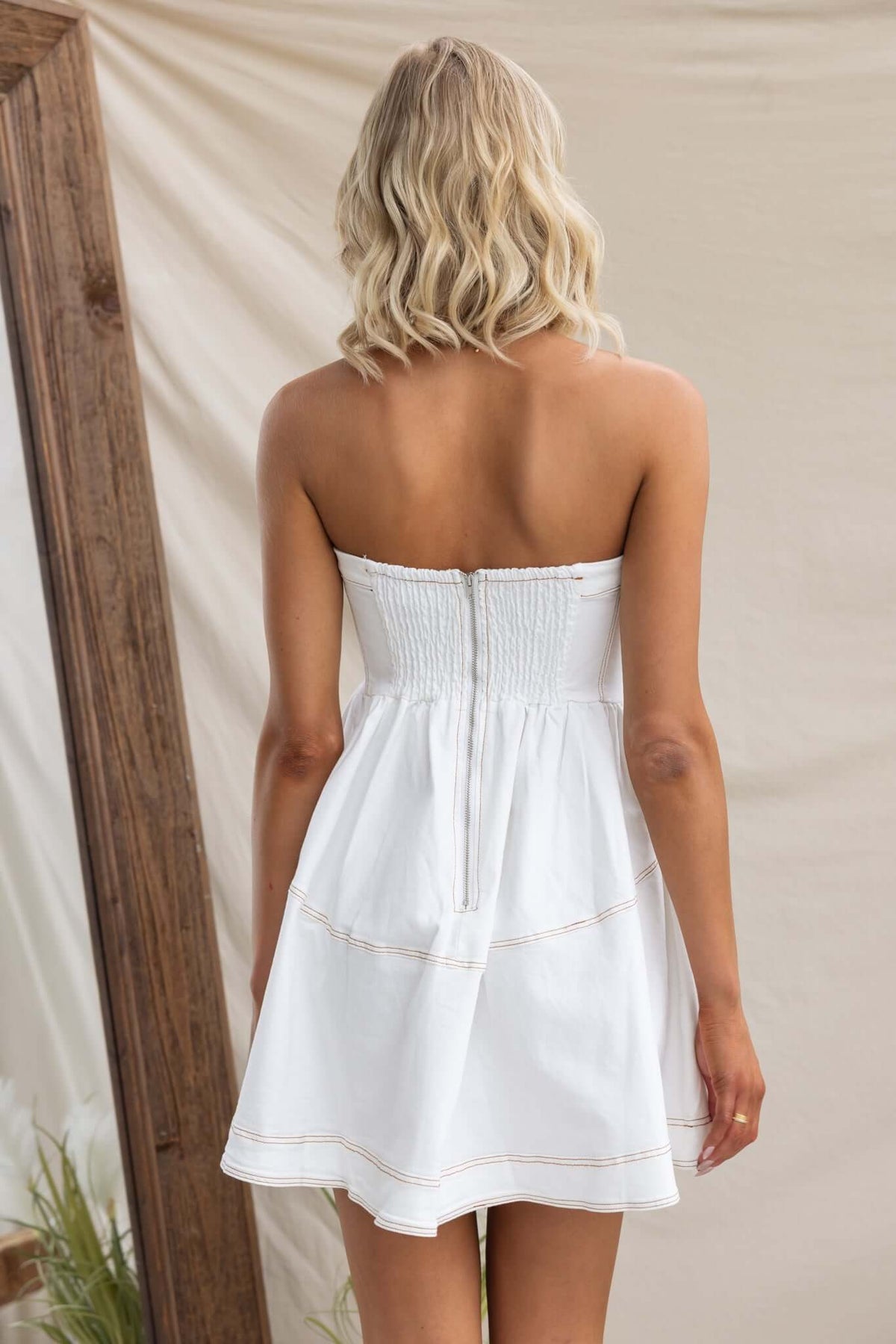 Model wearing a strapless white denim dress with back zip and elastic detailing, showcasing soft fabric and stylish fit.