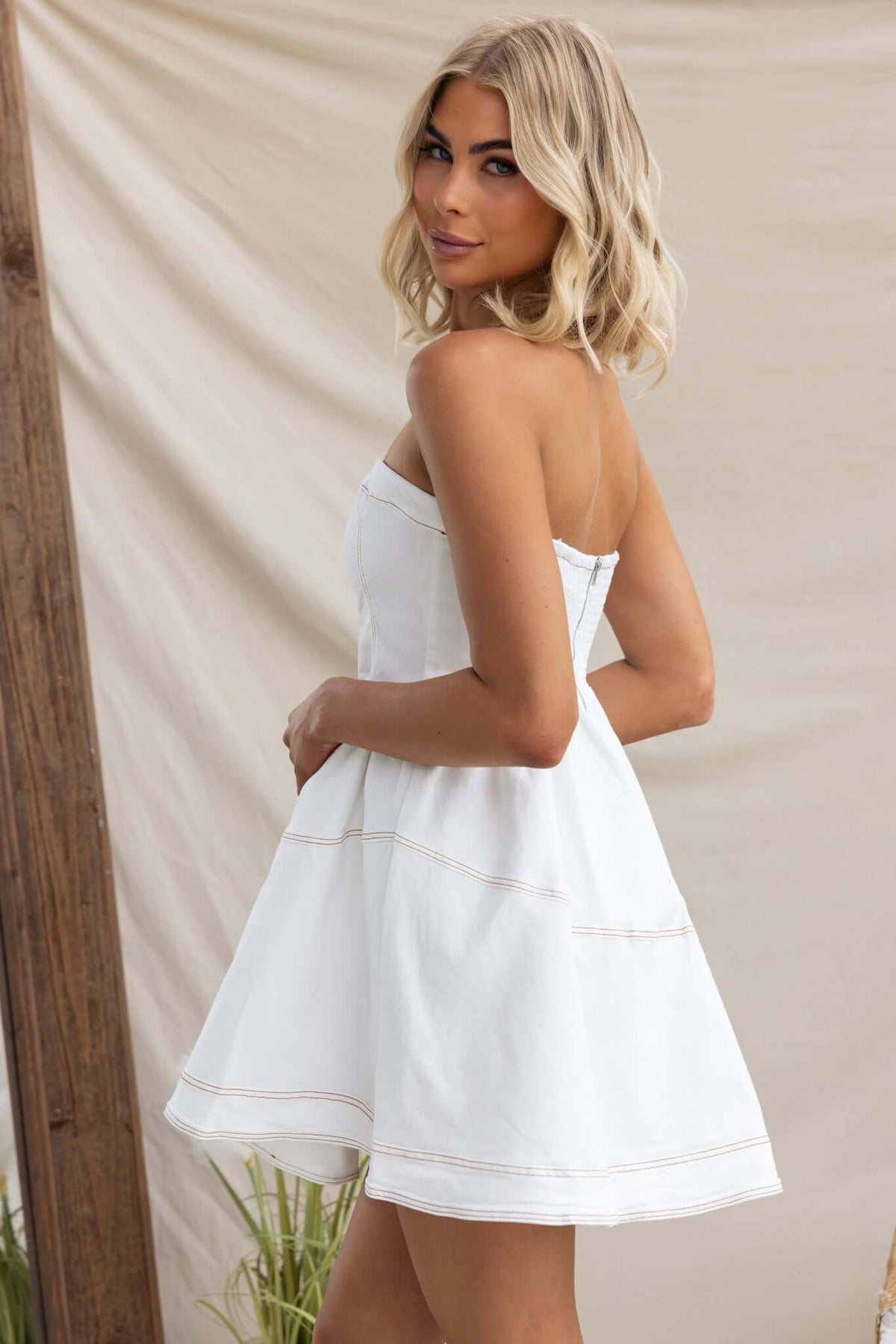 Model wearing a strapless Never Again Denim Dress in white, showcasing a soft denim feel and a flared silhouette.