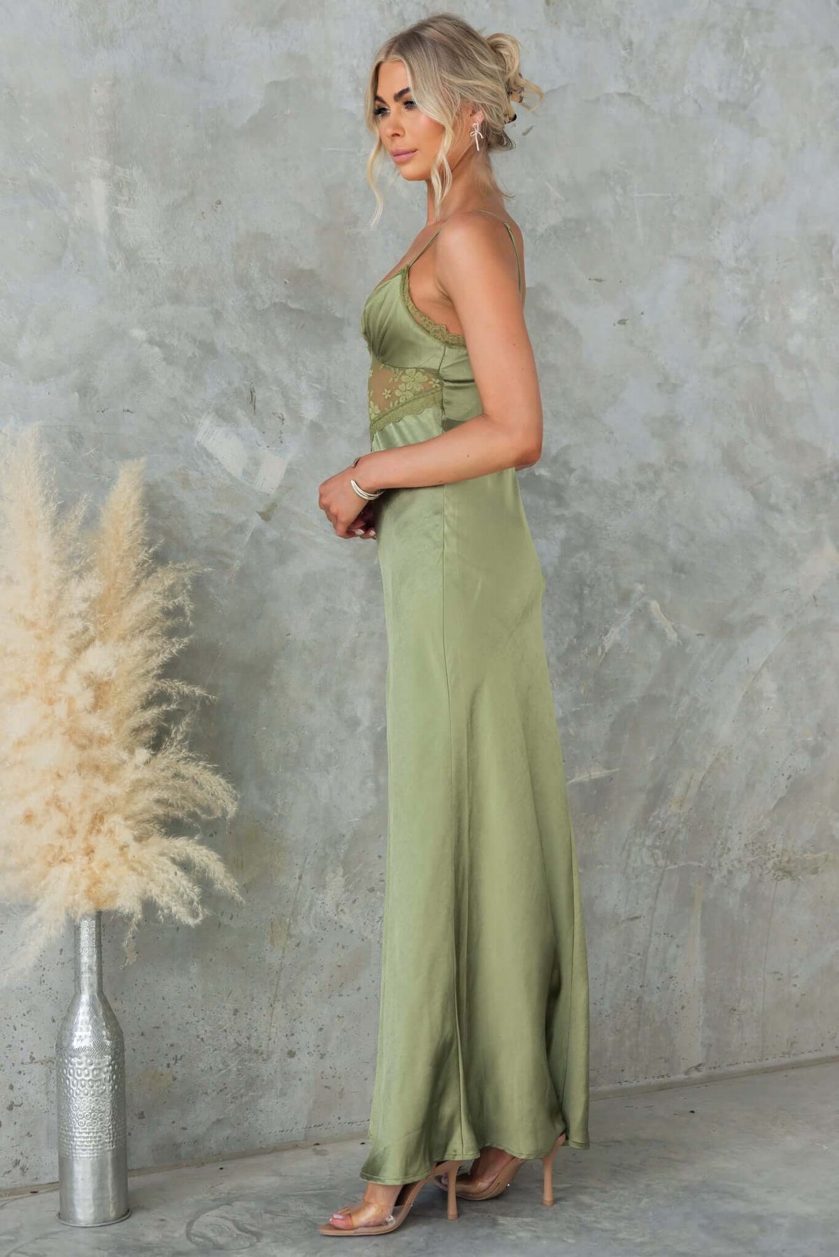 Model wearing a green Obsidian maxi dress with adjustable straps and lace panel, styled against a textured backdrop.