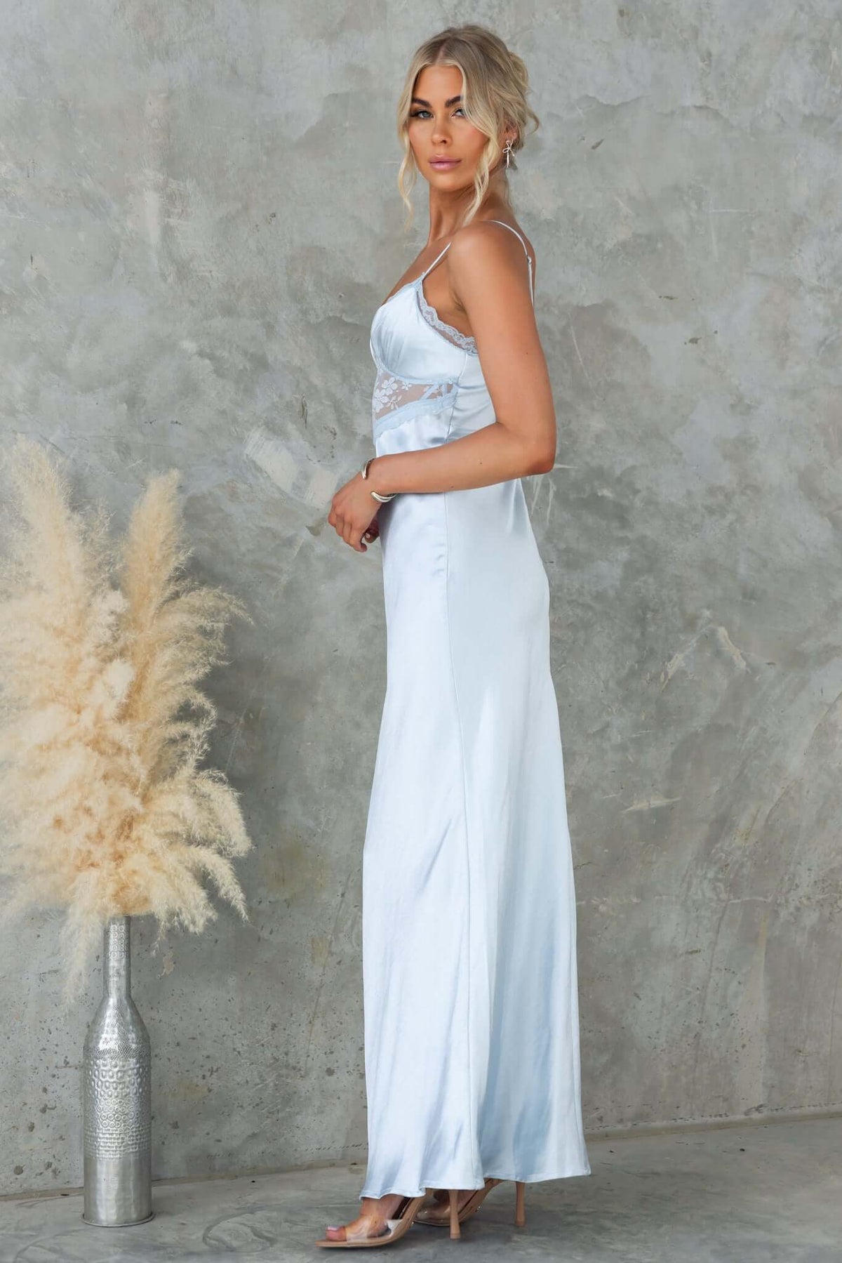 Elegant model in a light blue satin maxi dress with adjustable straps, styled with a floral backdrop.