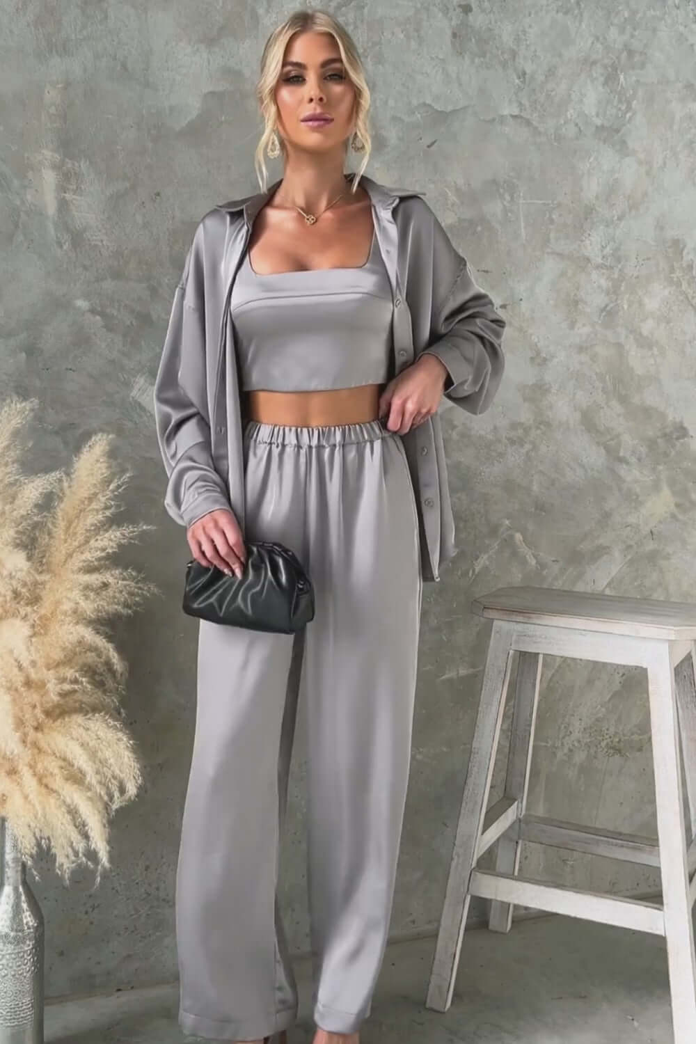 Kortez Pants: Satin mid-high waist pants with elastic waistband and pockets, styled with matching top, model in modern setting.