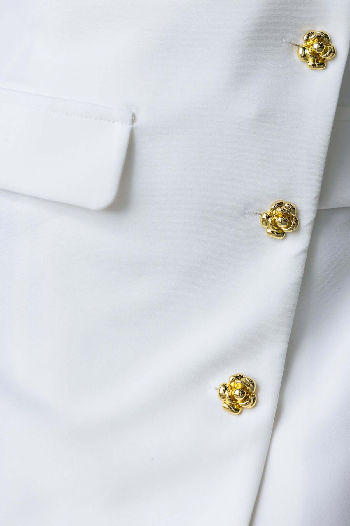 Close-up of Rhode Dress features, showcasing white fabric and gold flower buttons for a stylish look.