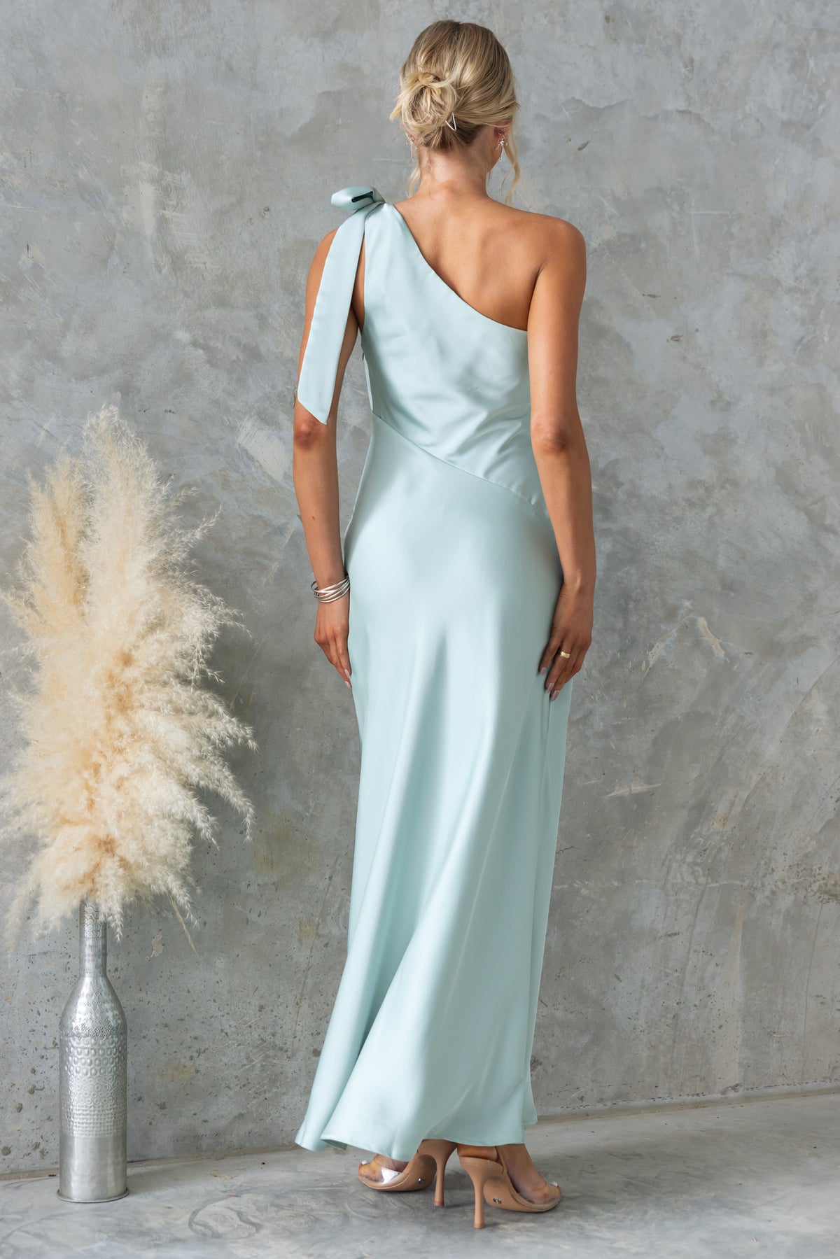 Back view of Ronnie Maxi Dress with one-shoulder tie neckline in satin, styled with elegant accessories.