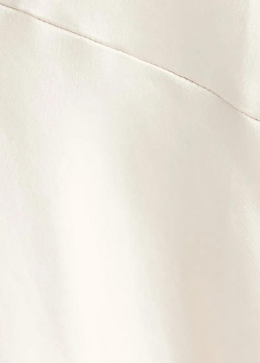 Close-up of draping satin material in creamy white, showcasing smooth texture and fine stitching details.