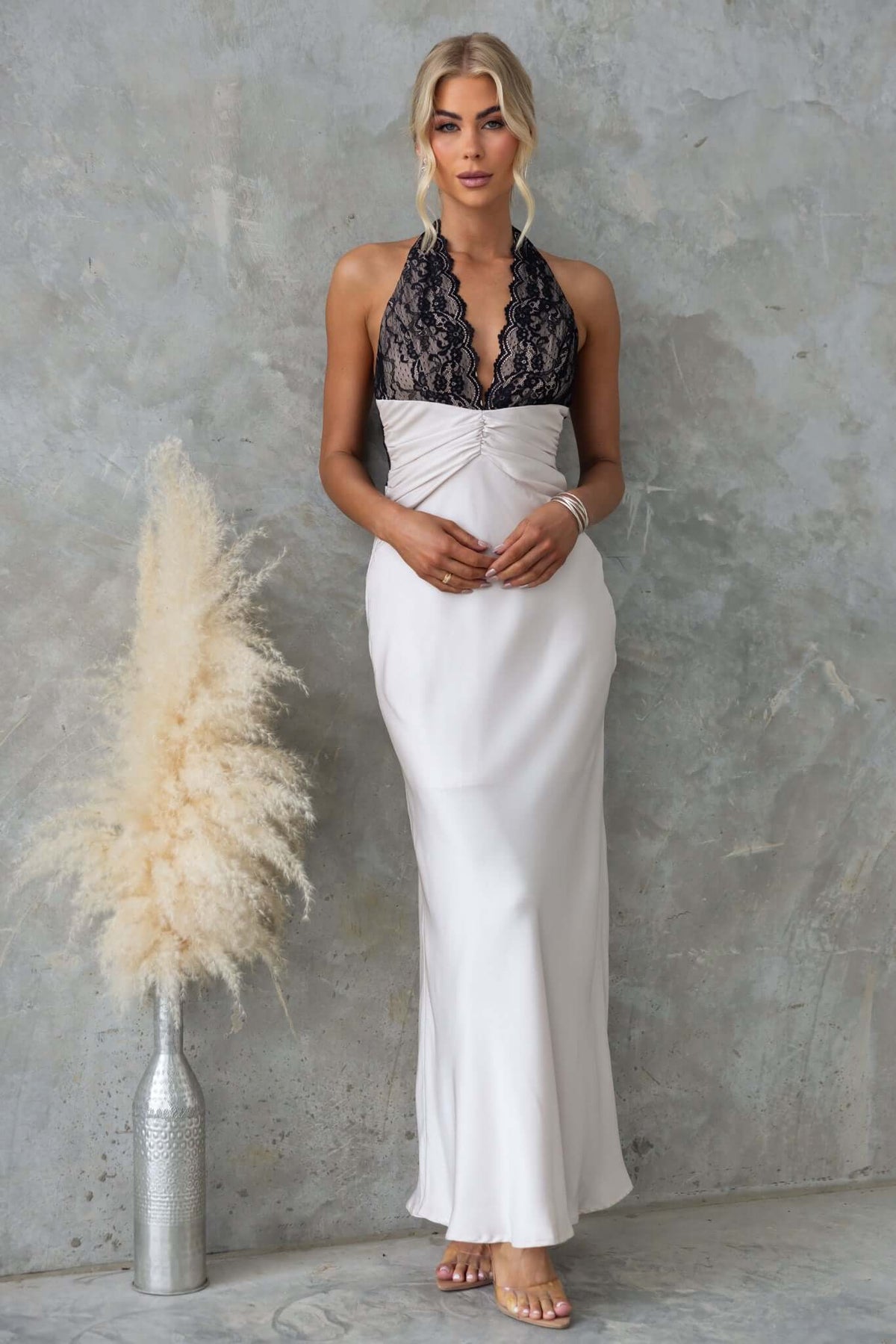 Model wearing the Sonrisa Maxi Dress with lace bust, tie neckline, and satin look, set against a textured backdrop.