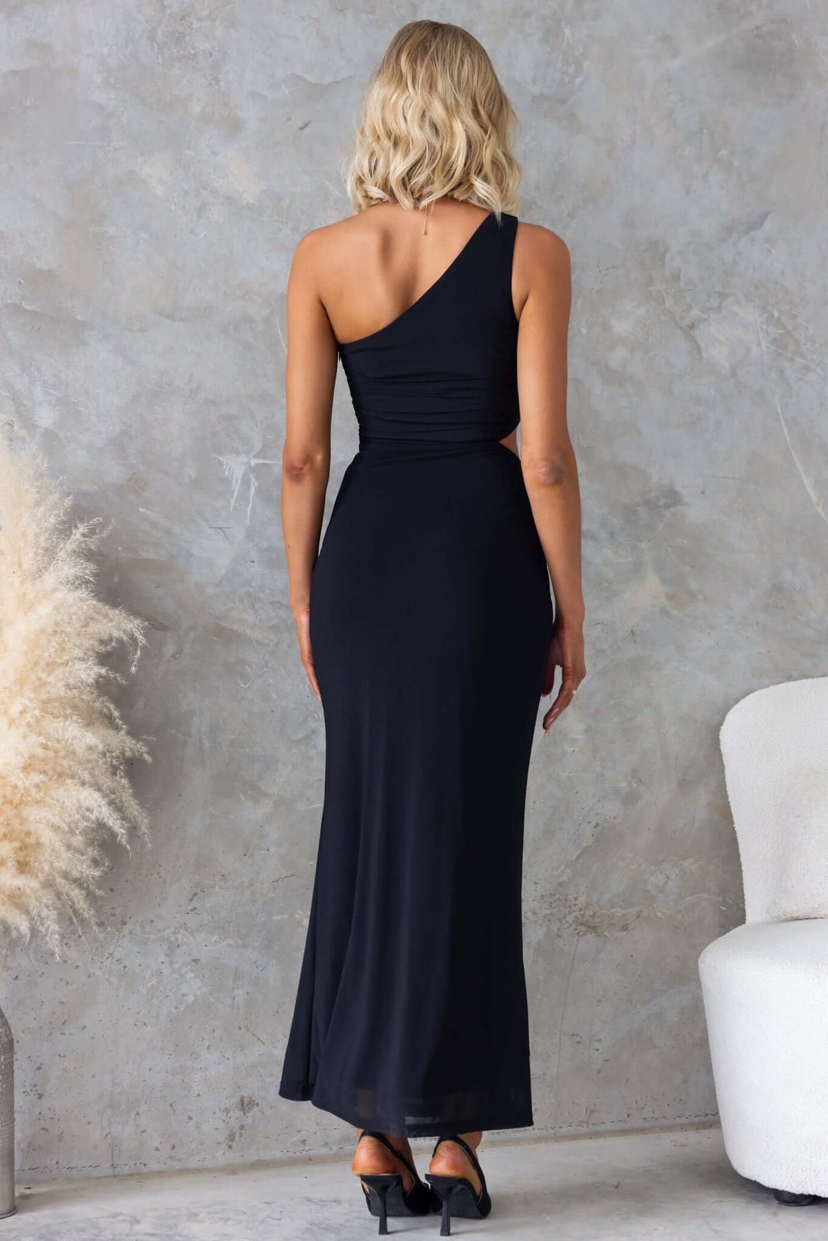 Back view of a stylish black ultra maxi dress with a one-shoulder neckline and waist cut-out, perfect for elegant occasions.
