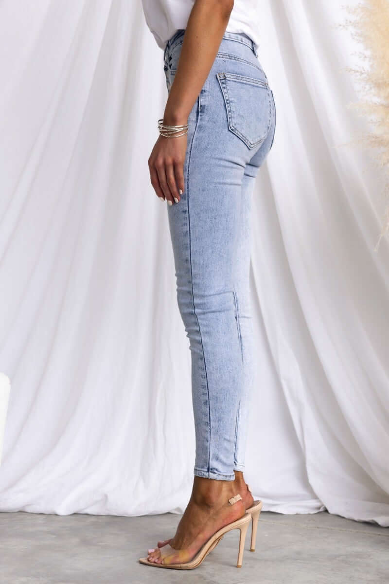 Side view of Under Cover Jeans showcasing mid-high waist, skinny fit, and light denim color, modeled with heels.