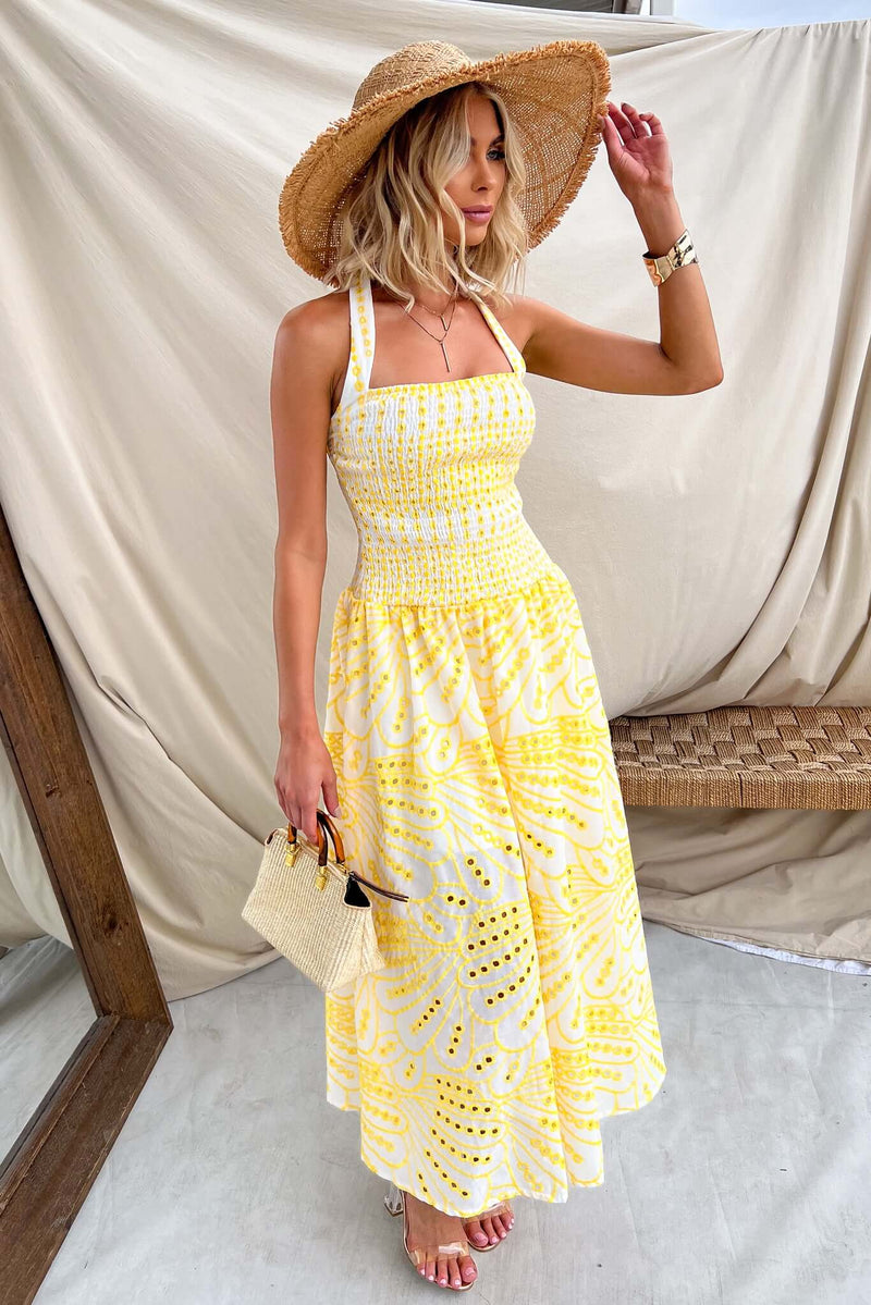 Model wearing Urena Midi Dress with halter neckline and Anglaise material, paired with a straw hat and stylish bag.