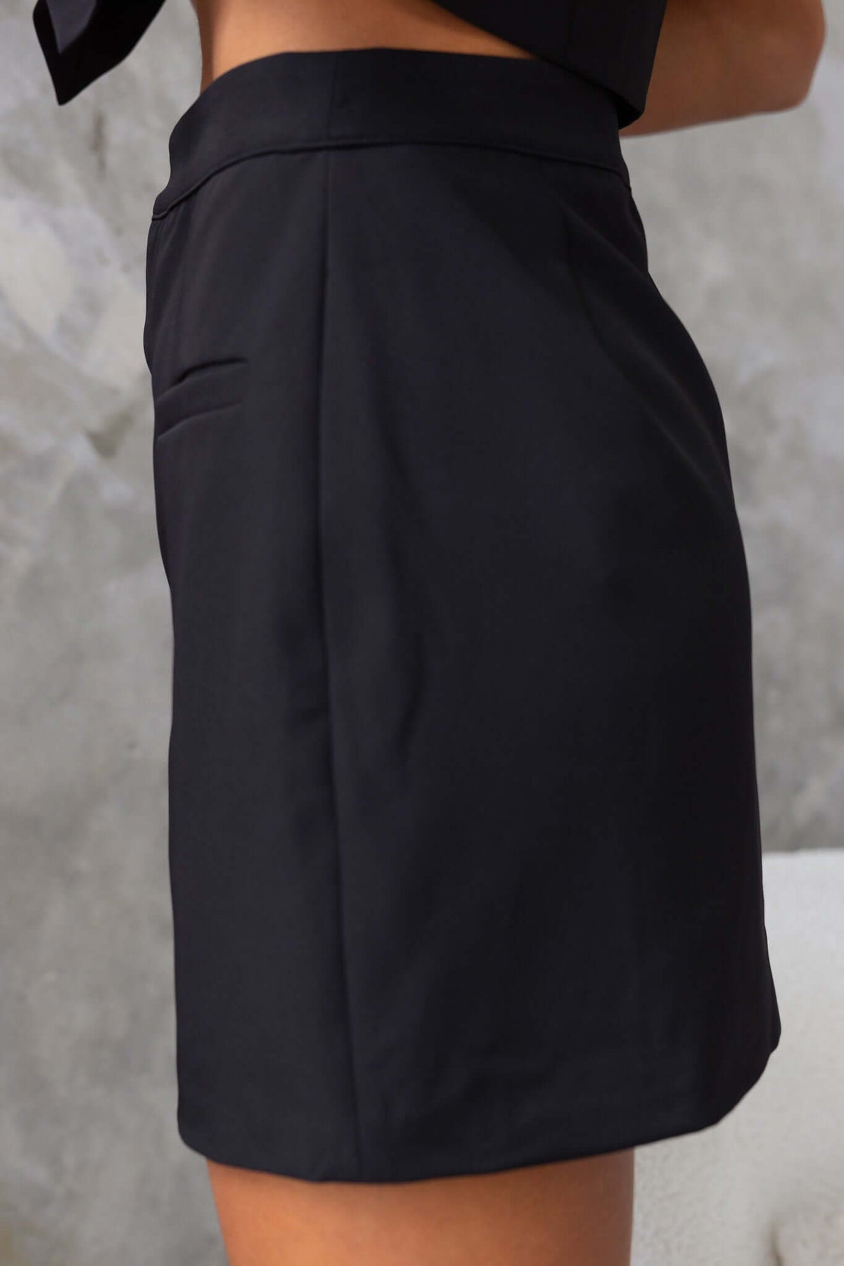 Side view of the Jayne Skirt, a mid-high waist black skirt featuring faux pockets and a sleek design.