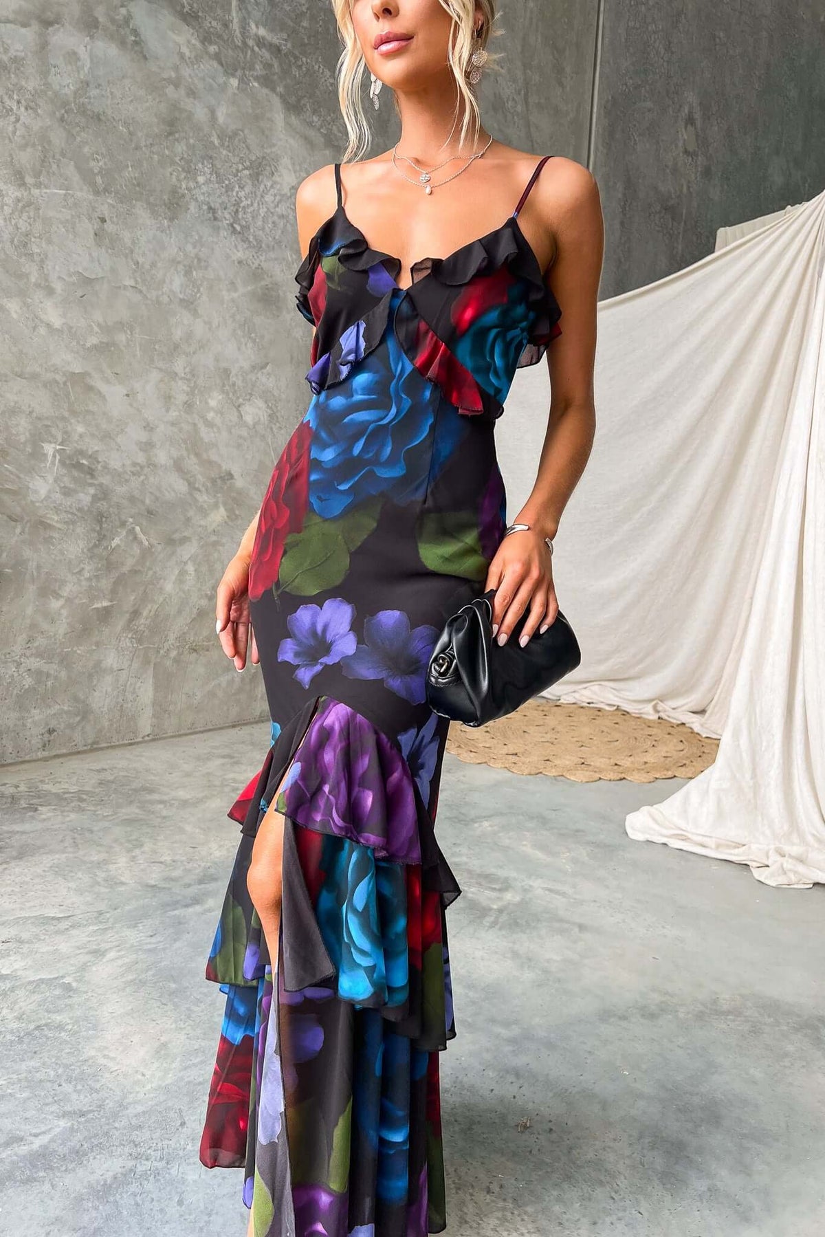 Black maxi dress with vibrant floral prints, adjustable straps, ruffles, and front split, perfect for summer occasions.