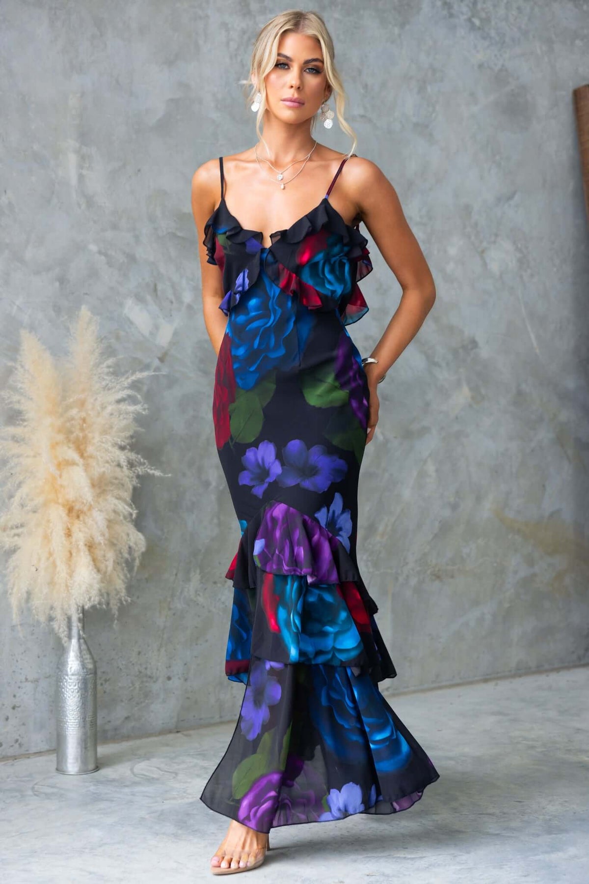 Model wearing a floral ruffle maxi dress with adjustable straps and split front, showcasing vibrant colors on chiffon fabric.