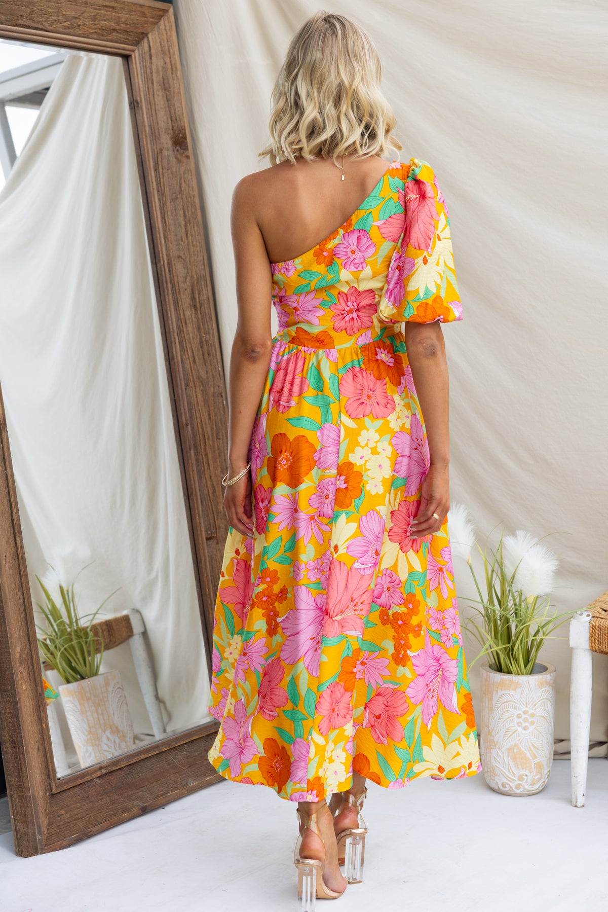 Back view of Woran Midi Dress featuring vibrant floral print and one-shoulder design, styled with strappy heels.
