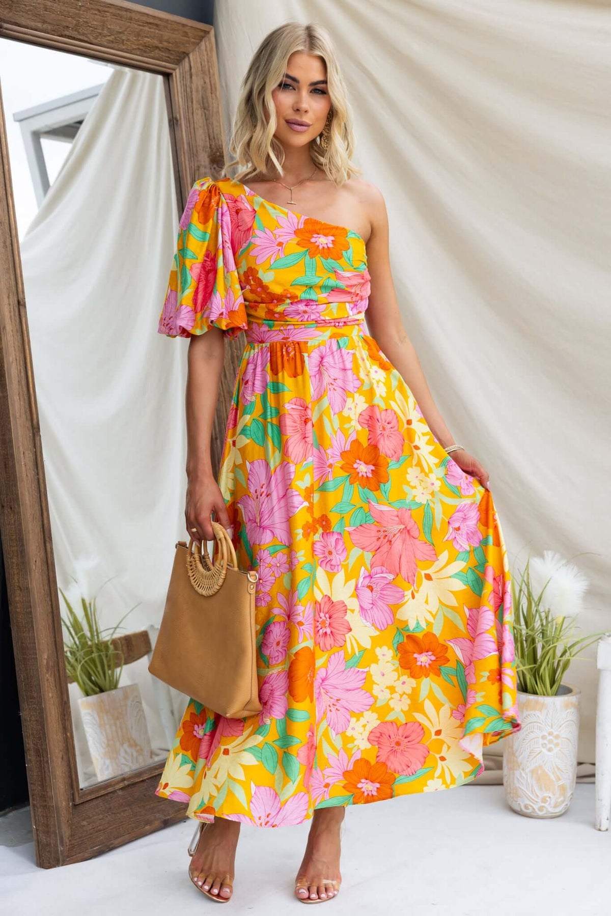 Colorful floral print Woran midi dress featuring one-shoulder neckline and flowy skirt, styled with a tan handbag.