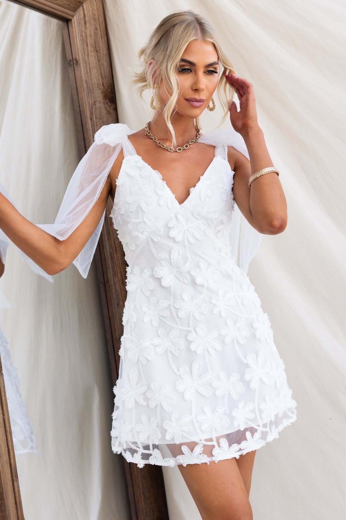 Xaria dress in white with embroidered flowers and tie straps, modeled by a woman with long hair.