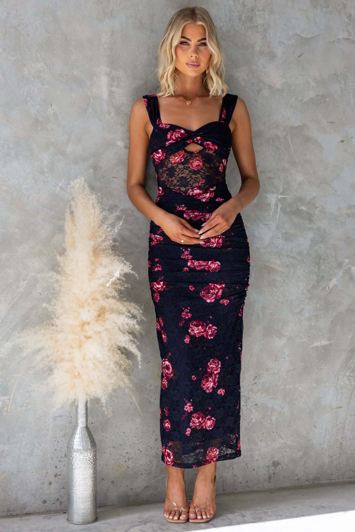 Model wearing Xavina Maxi Dress in navy with floral design, twist detail, and cut-out at bust, styled against a textured background.