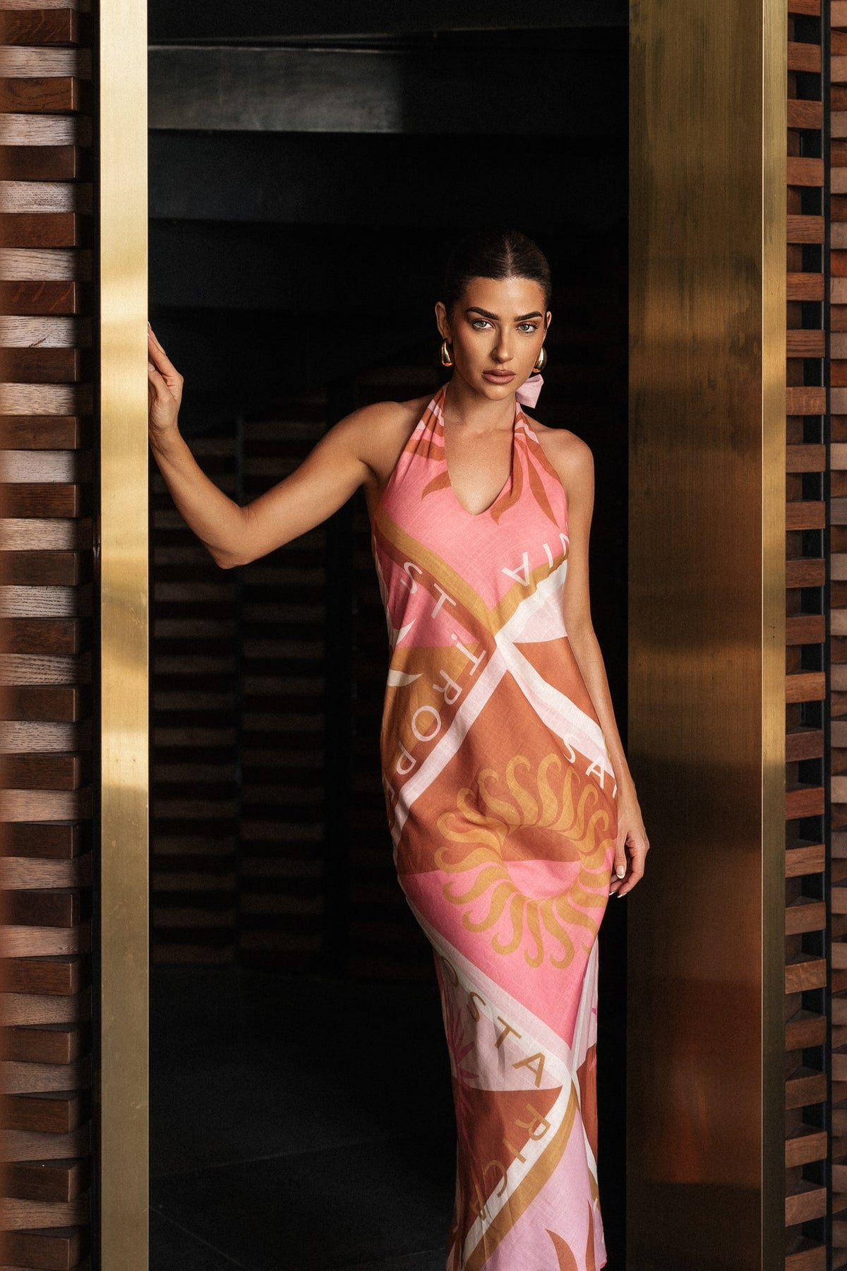 Jovie Maxi Dress in a vibrant print, featuring adjustable tie neckline and low-cut back, styled in an elegant setting.