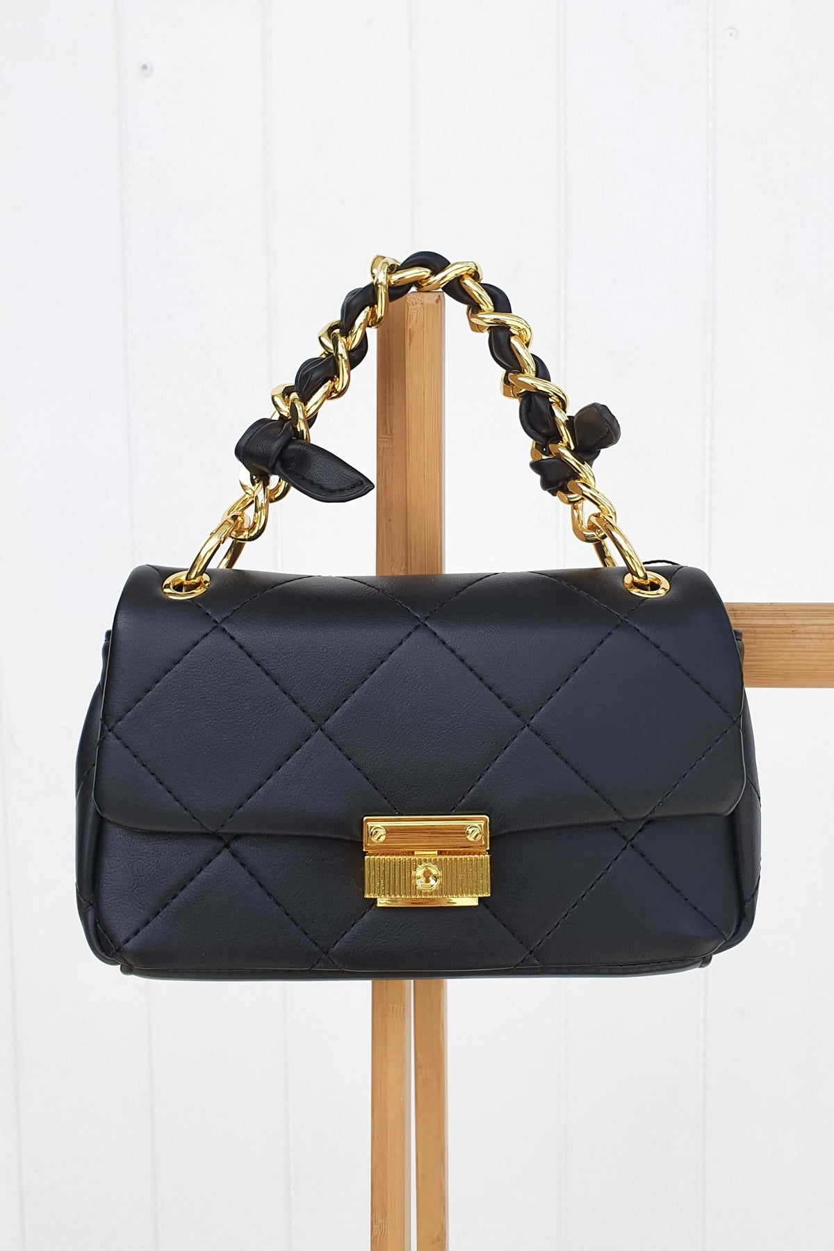 Ari Bag featuring a sleek black vegan leather exterior, quilted design, and a gold chain handle with clasp.