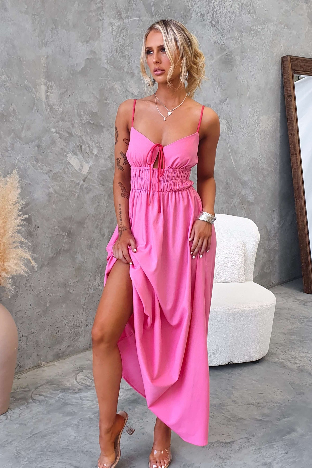 Brooklynn Maxi Dress in pink with adjustable straps and a tie front, featured in a stylish indoor setting.