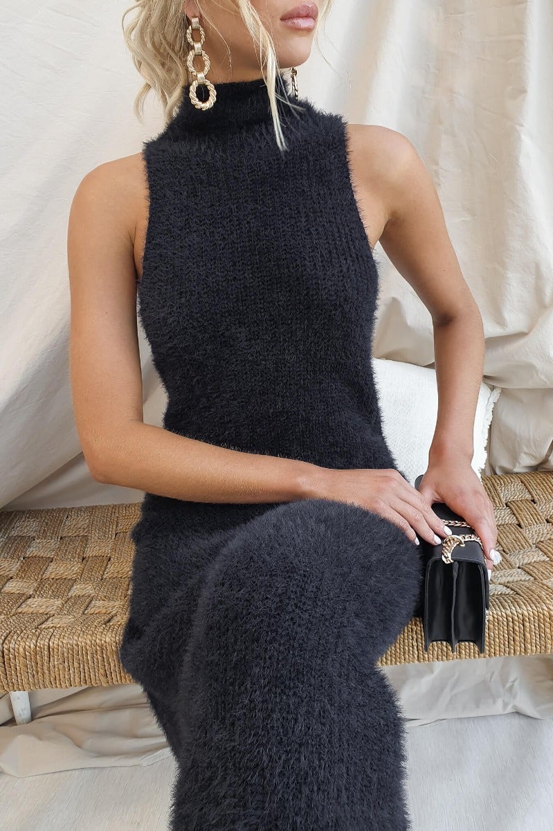Black fluffy knit maxi dress with high neckline, model styling with accessories in a cozy setting.