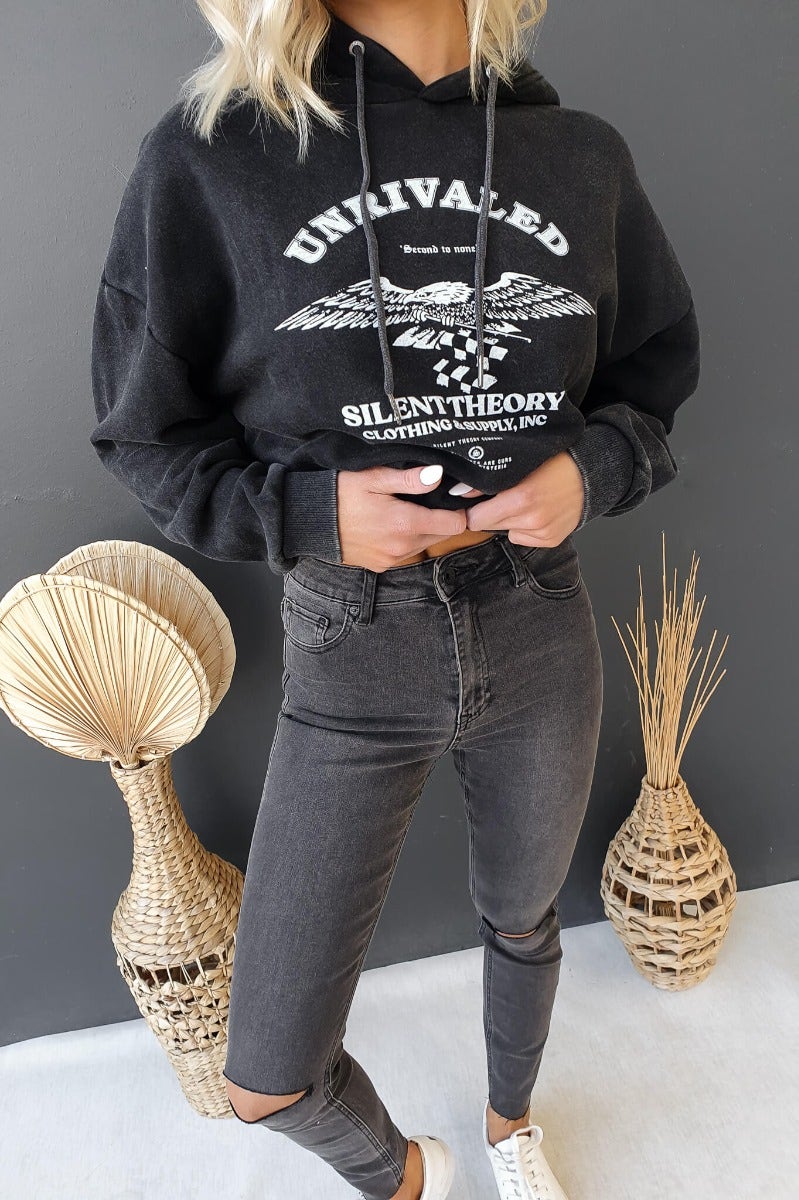 Ivar jumper in washed black with hood, featuring 'Unrivaled' print, styled with high-waisted jeans.