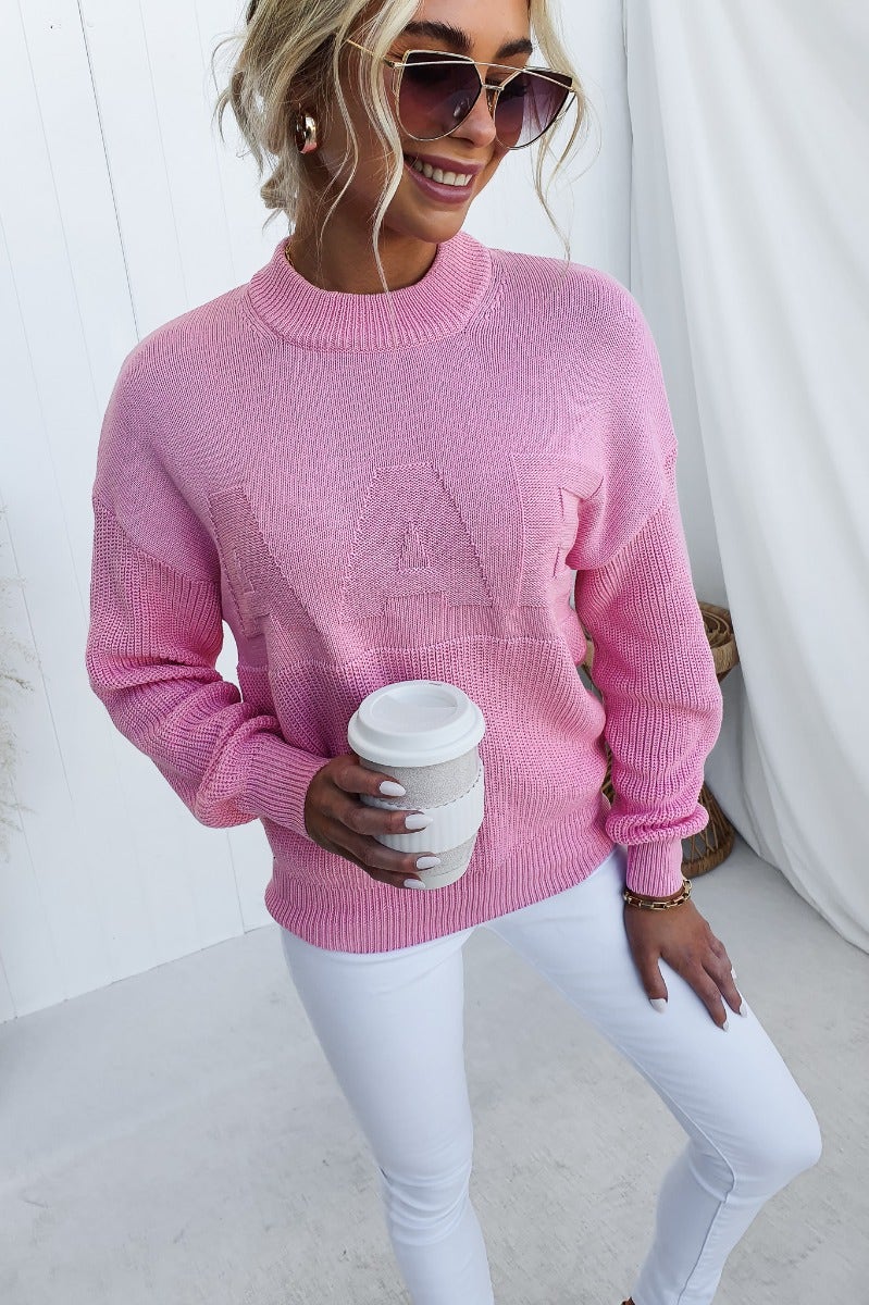 Raymer Jumper in pink, featuring embossed 'AAE', round neckline, worn by model with coffee cup.