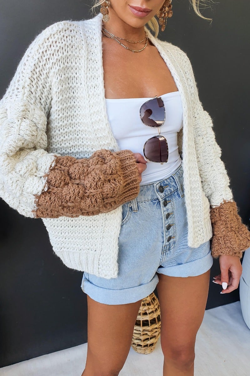 Model wearing Qira Cardigan with chunky sleeves, styled with a white tank top and high-waisted denim shorts.