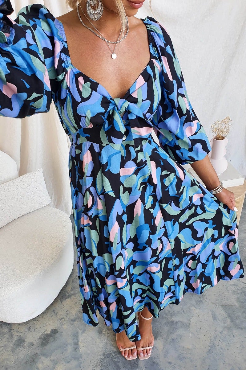 Clemence Midi Dress featuring colorful floral print, tie bust detail, and puff sleeves, perfect for casual or semi-formal occasions.