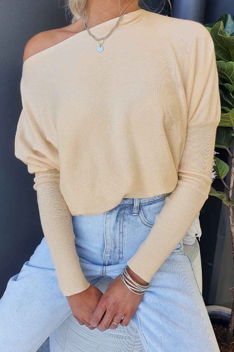 Woman wearing a cosy oversized Bonnie Knit top in beige, paired with high-waisted jeans and layered jewelry.