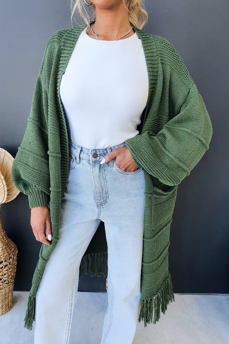 Zeddie Cardigan in green, featuring a longline fit, pockets, and a relaxed style worn with jeans.