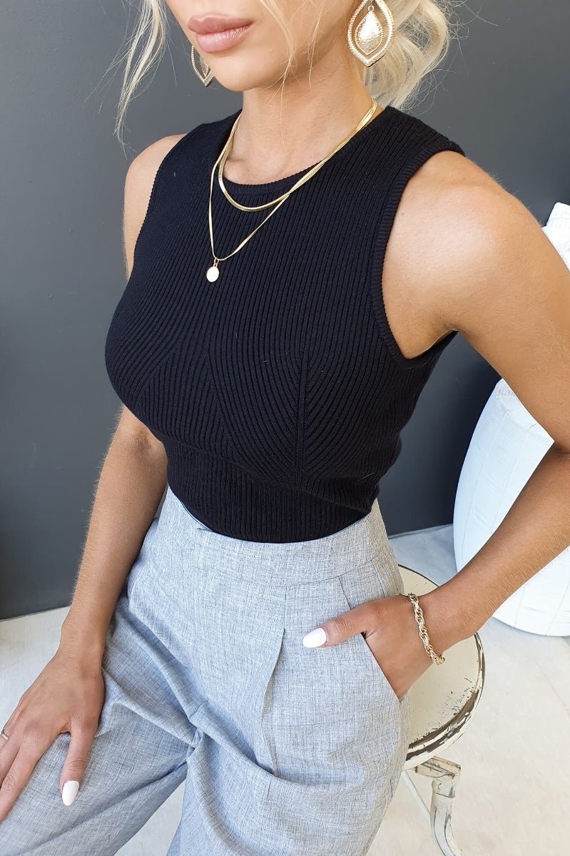 Morgan Top in black ribbed material with high neckline, paired with grey trousers, showcasing stylish fit and elegant accessories.