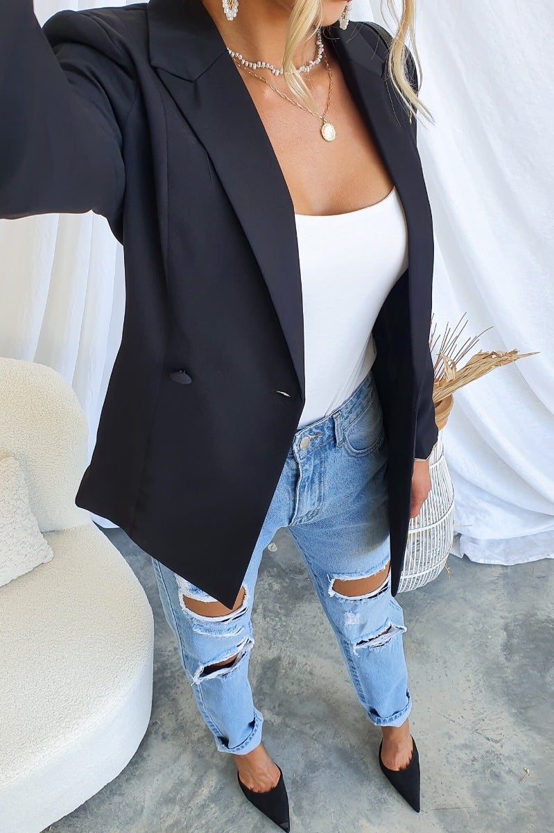 Chic black Zeva blazer styled with a white top and ripped jeans, showcasing its tailored fit and sophisticated design.