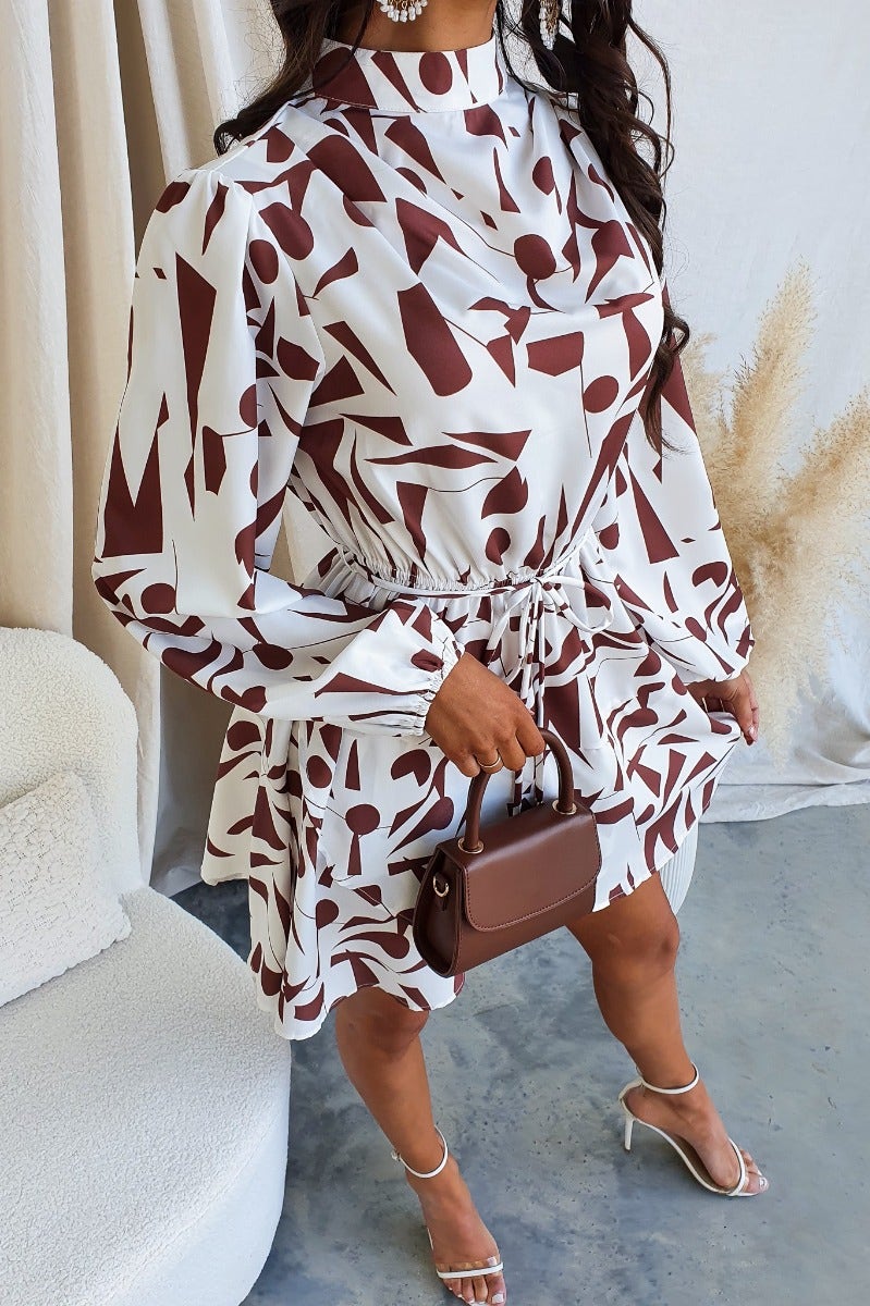 Model in Eleyna Dress featuring a multi-colour print, high neckline, elastic waist, and removable tie.
