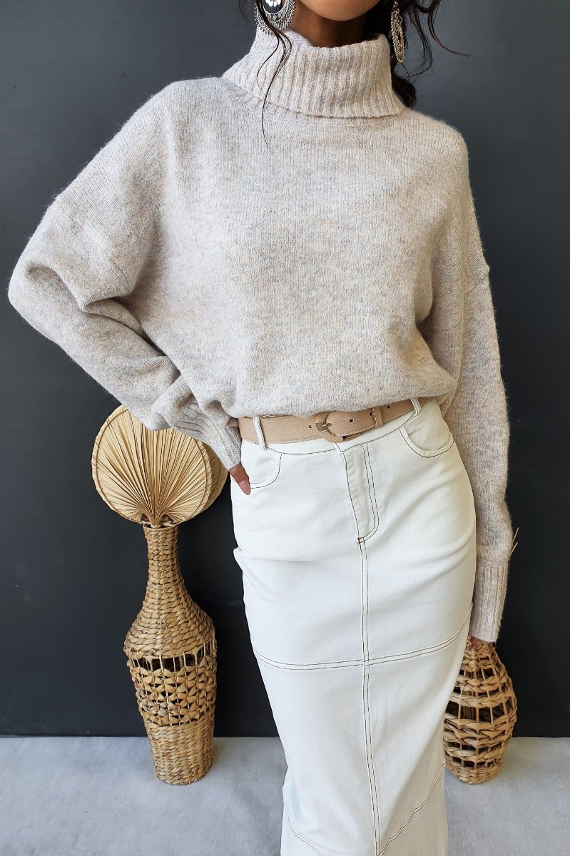 Chic Orion jumper with turtle neckline, relaxed fit, and beige color, styled with a white skirt and accessories.