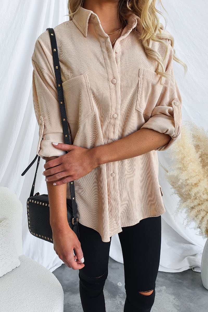 Woman wearing a relaxed fit stone corduroy shirt with button-up front and pockets, paired with a stylish handbag.