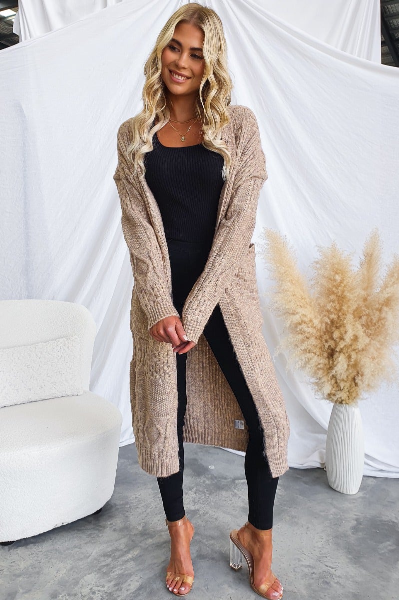 Emerson cardigan in cable knit style, longline fit with pockets, paired with black outfit and sandals.